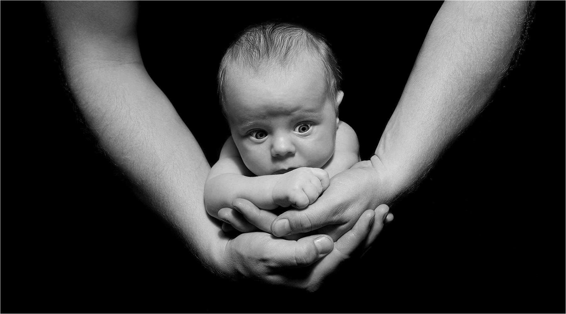  Schwangeren & Babyfotografie. Aussergewöhnlich schöne LowKey Aufnahme als Kinderportrait in den Händen des Vaters. Geborgenheit pur. Aufgenommen mit digital Mittelformattechnik und Studioblitzanlage im Fotostudio Riethausen.  Copyright by Fotostudio Jörg Riethausen 