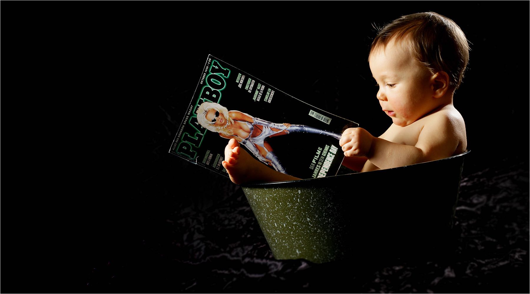 Schwangeren & Babyfotografie. Witziges Portrait eines Kleinkindes mit einer Erwachsenen Zeitschrift in einer Blechwanne sitzend. Studioaufnahme vor dunklem Hintergrund. Copyright by Fotostudio Jörg Riethausen 