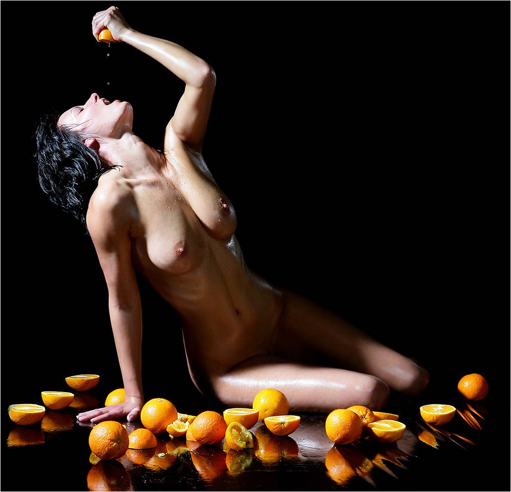  Junge nackte Frau presst eine Orange aus und trinkt den Saft. Auf Spiegelfolie sitzend im schwarzen Studio, fotografiert mit Kleinbild digital. Copyright by Fotostudio Jörg Riethausen 
