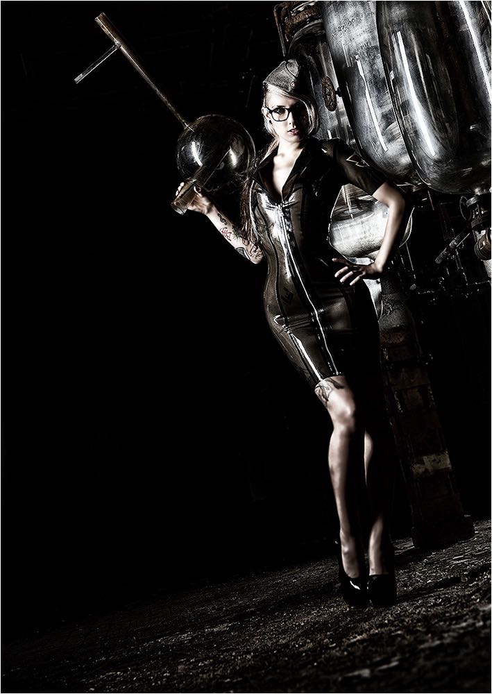  On Location Aufnahme eines Models im Latexkleid und aussergewöhnlichem Glasbehältnis als Waffe über der Schulter. Fotografiert mit mobiler Studioblitzanlage in einer verlassenen Fabrik mit Kleinbild Digitalkamera. Copyright by Fotostudio Jörg Riethausen 