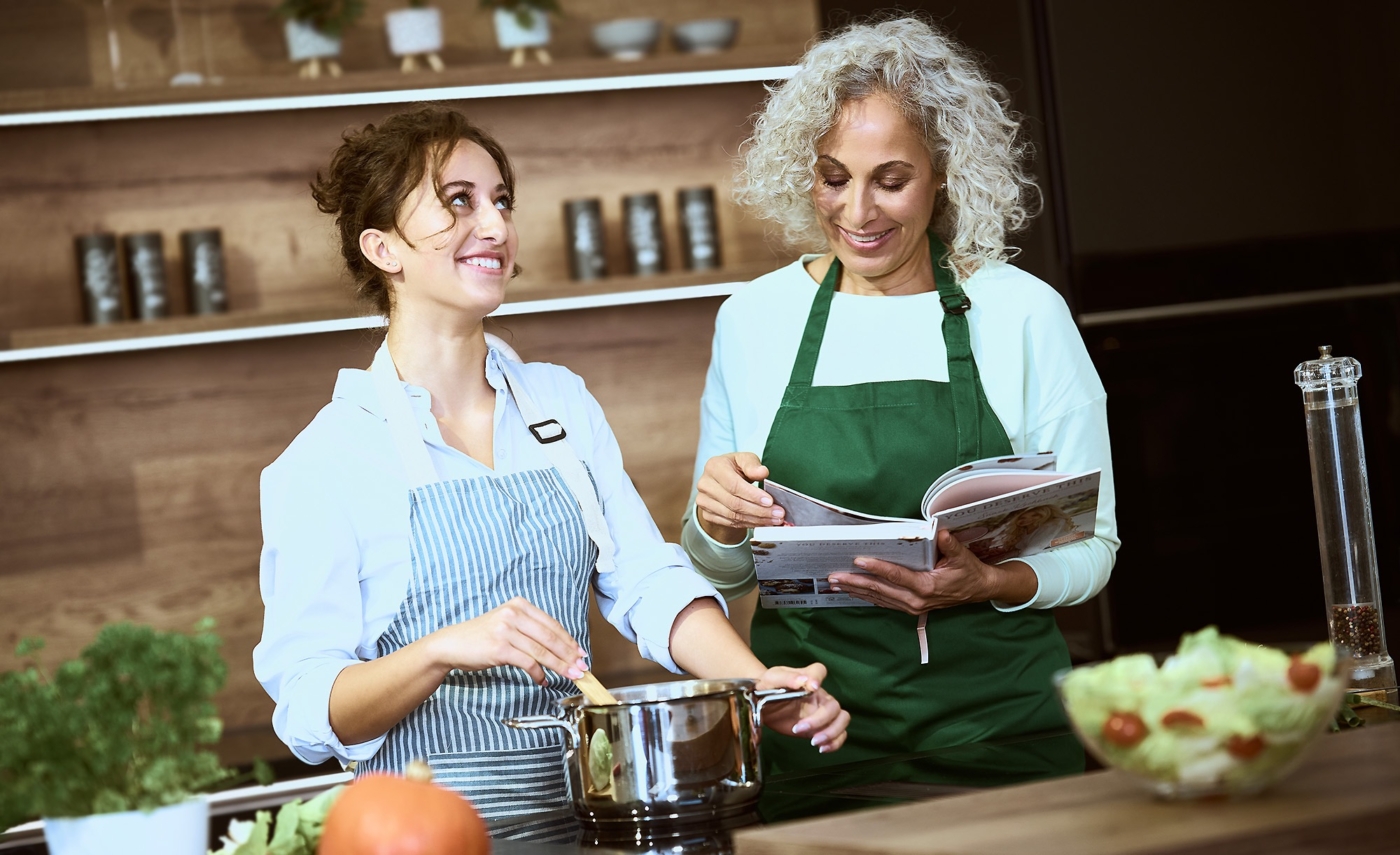Mutter und Tochter beim Kochen. Tochter rührt die Suppe und die Mutter liest im Kochbuch