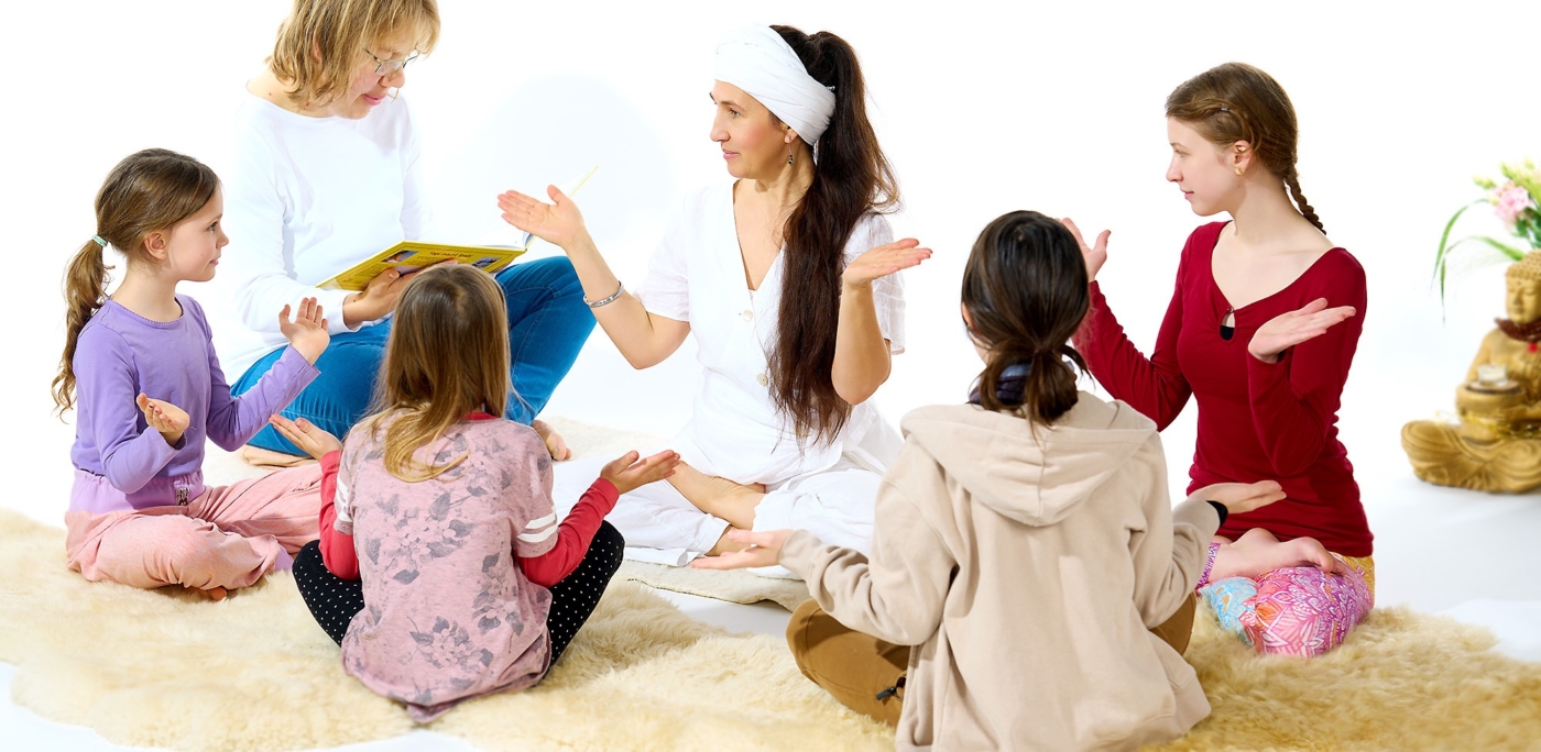 Kinder beim Yoga mit Yogalehrerin in weissem outfit alle sitzend auf Schaffellen