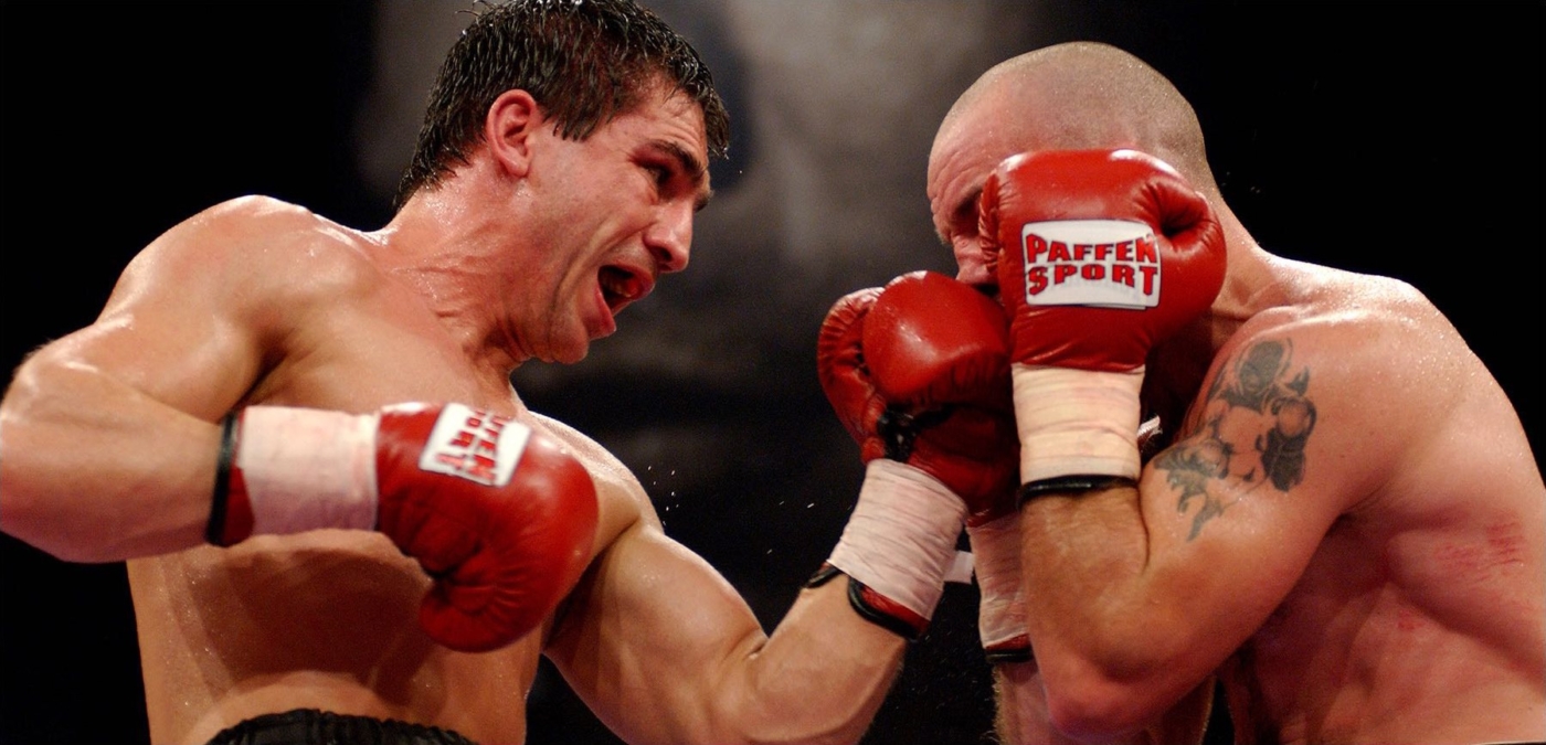 Zwei Boxer mit roten Handschuhen im Kampf. Einer trifft die Nase des anderen