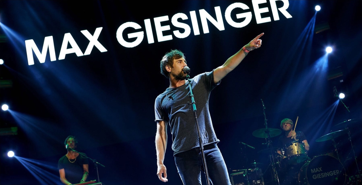 Sängerportrait Max Giesinger während eines Auftrittes mit ausgestrecktem Arm