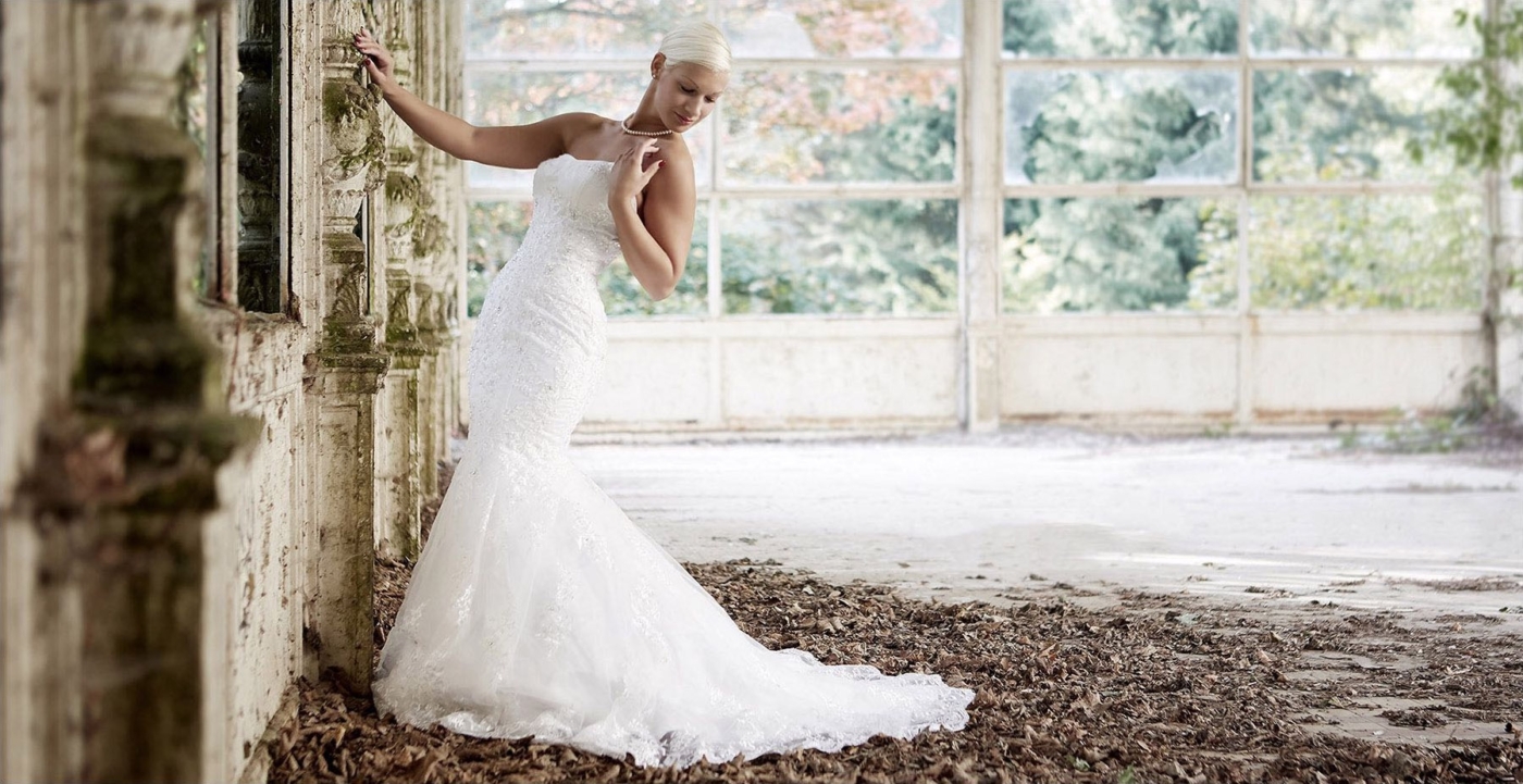 Blonde Frau im Brautkleid in einem verlassenen Schlossgarten