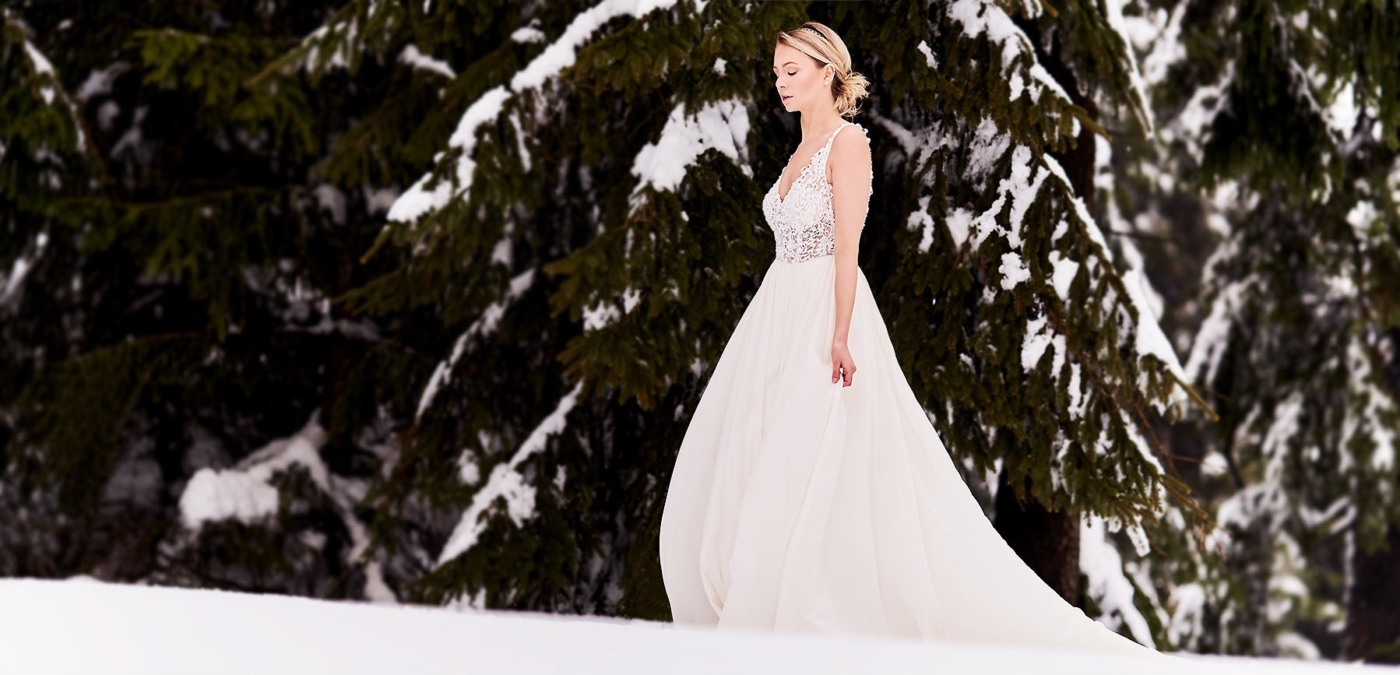 Frau im weissen Brautkleid im verschneiten Winterwald mit gesenktem Blick