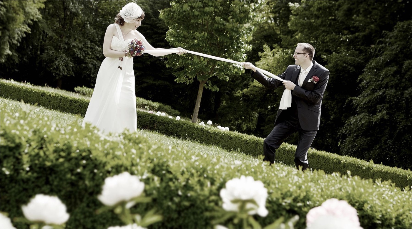 Das Brautpaar beim Tauziehen mit den Brautschal in einem grünen Park
