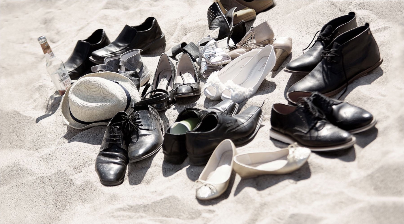 Männer und Damenschuhe im Sand und eine Flasche Bier