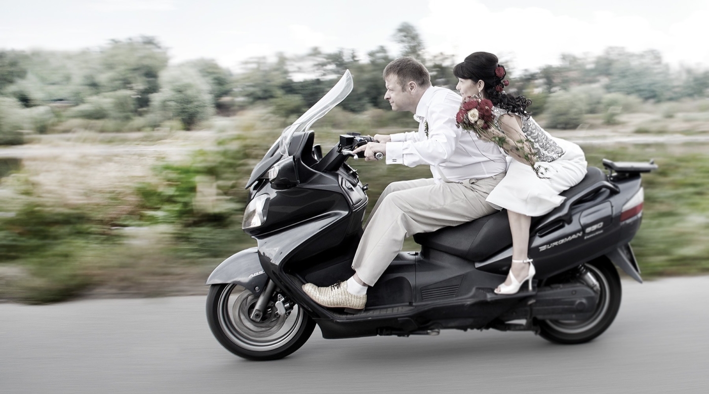 Braut und Bräutigam auf einem Moped in rasanter Fahrt durch die Landschaft