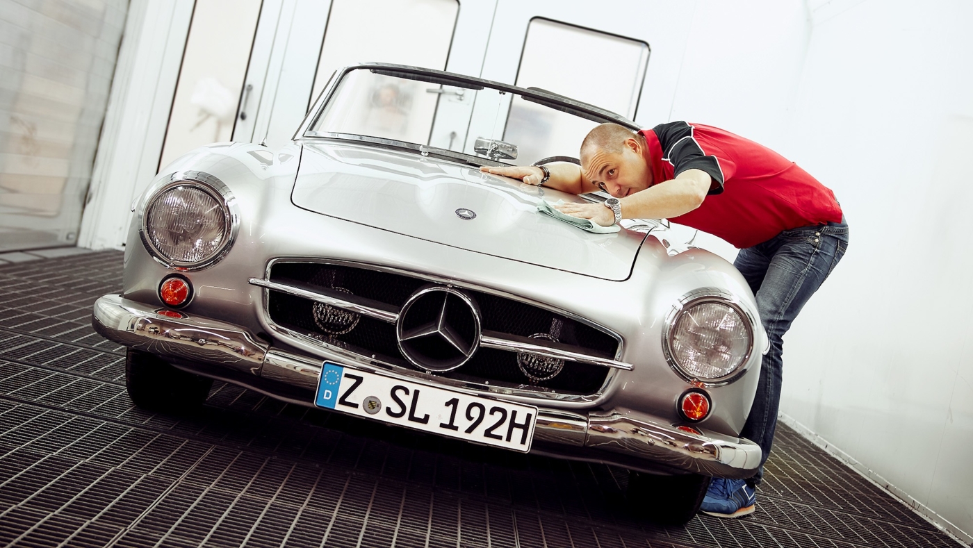 Autolackierer prüft das Ergebnis seiner Arbeit an der Motorhaube an einem alten Mercedes Cabrio