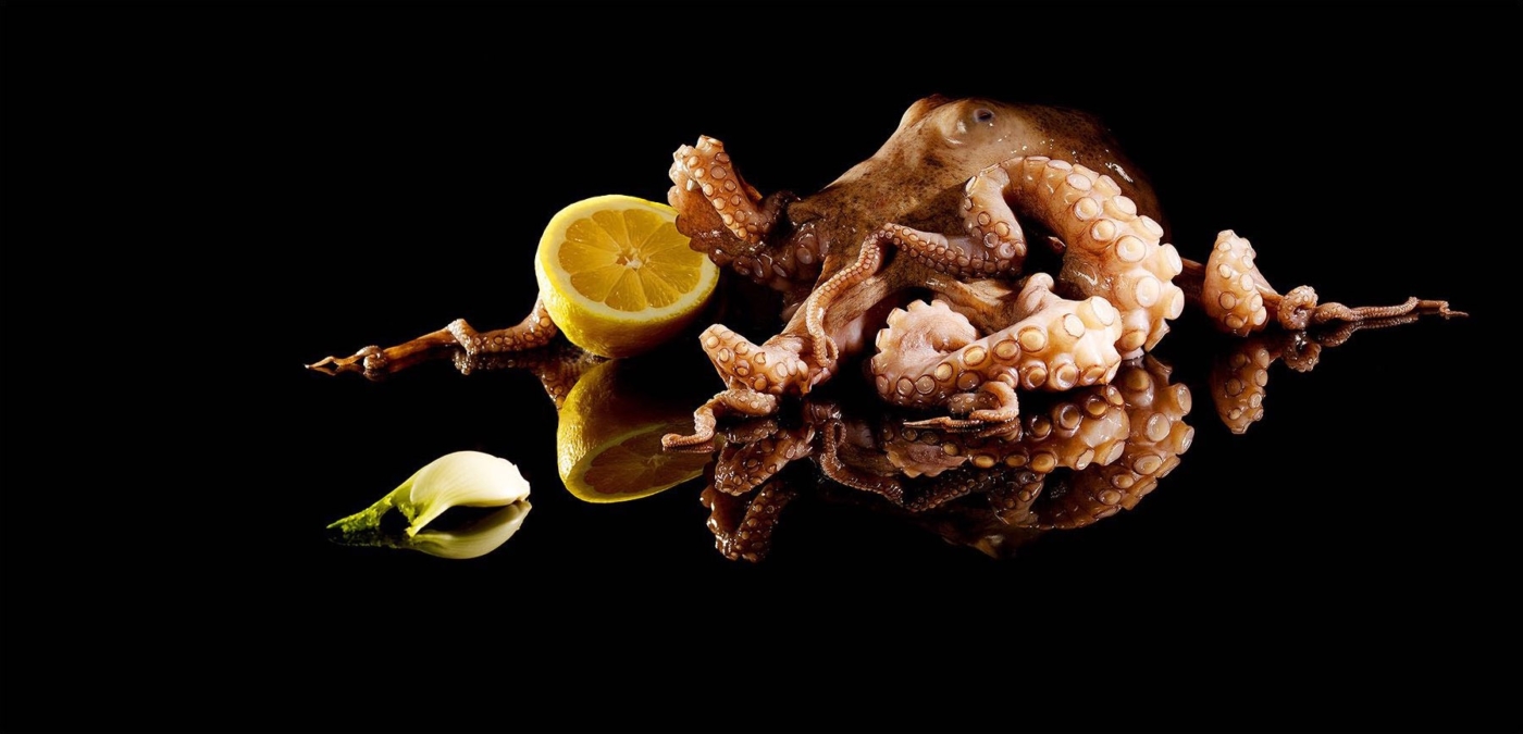 Ein Pulpo liegend auf schwarzem Glas und schwarzem Hintergrund mit Zitrone und Fenchel