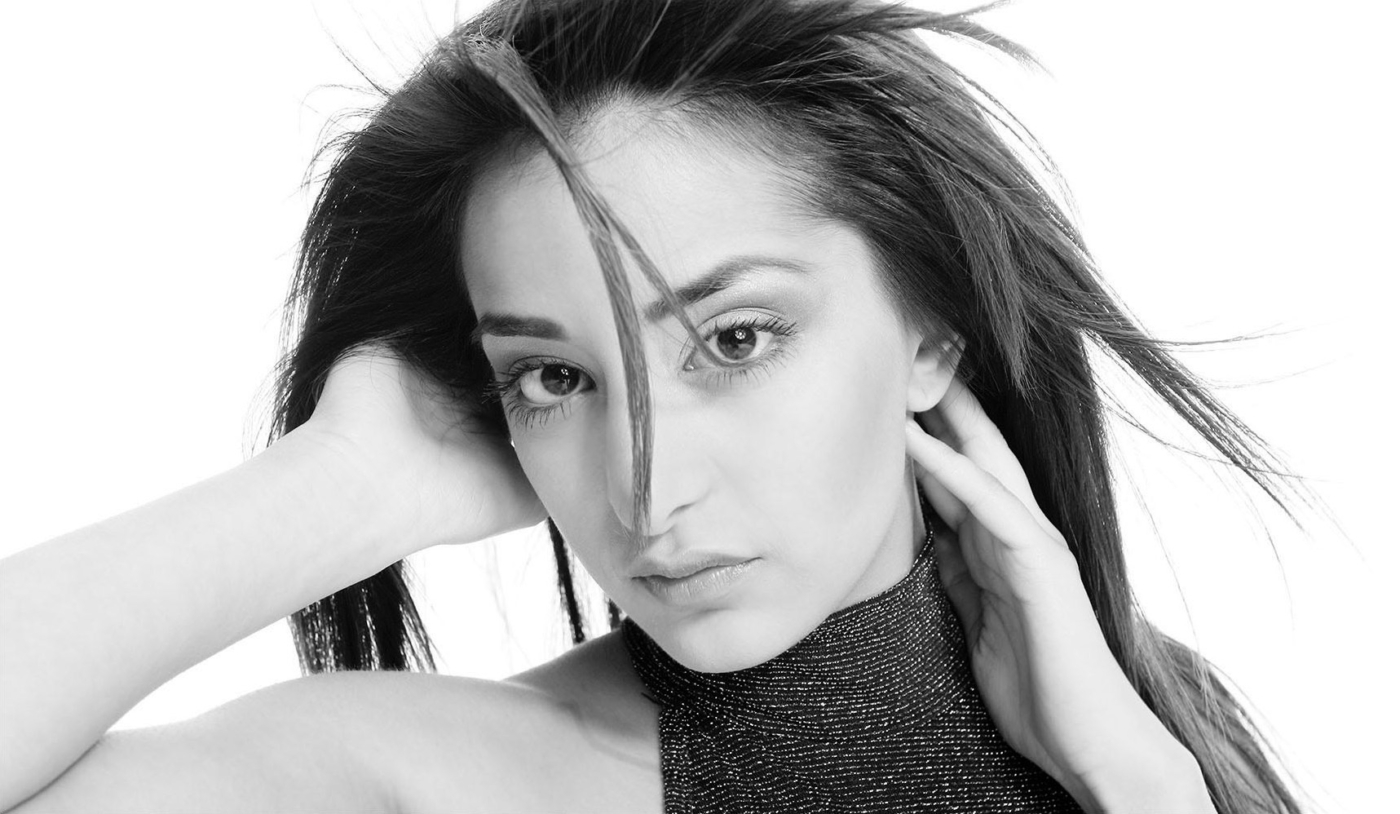 Nahaufnahme Gesicht einer Frau mit dunklem glatten Haar und Händen am Kopf in Schwarz weiss