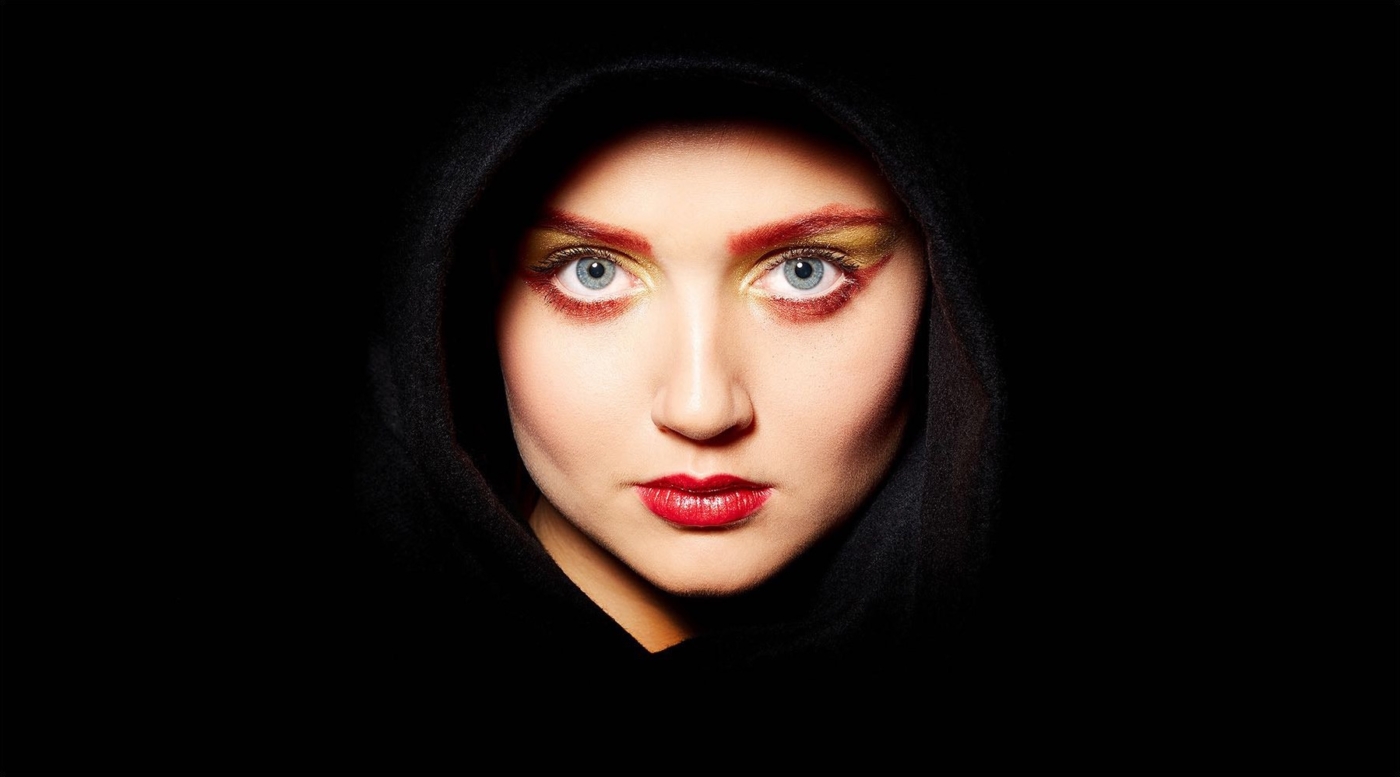 Nahaufnahme des Gesichtes einer jungen Frau mit schwarzem Tuch um den Kopf und schwarzem Hintergrund