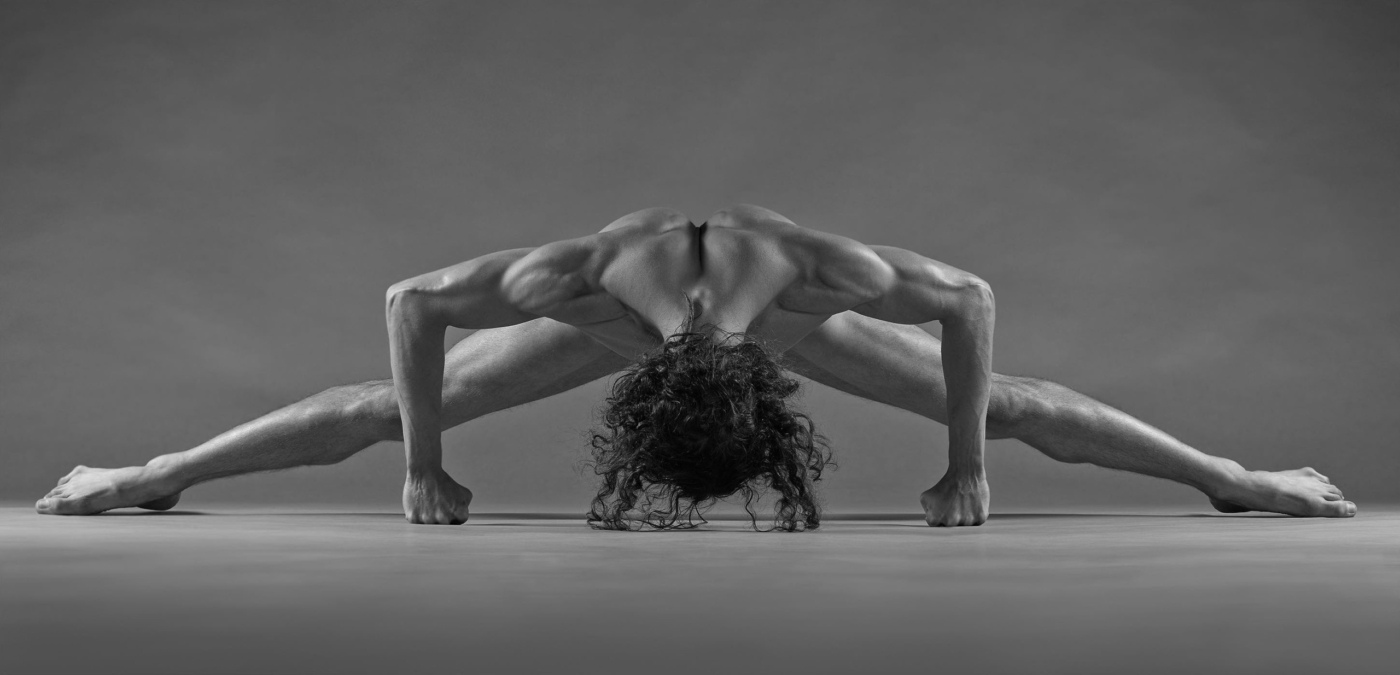 Verdeckter muskulöser Männerakt im Spagat vor grauem Hintergrund