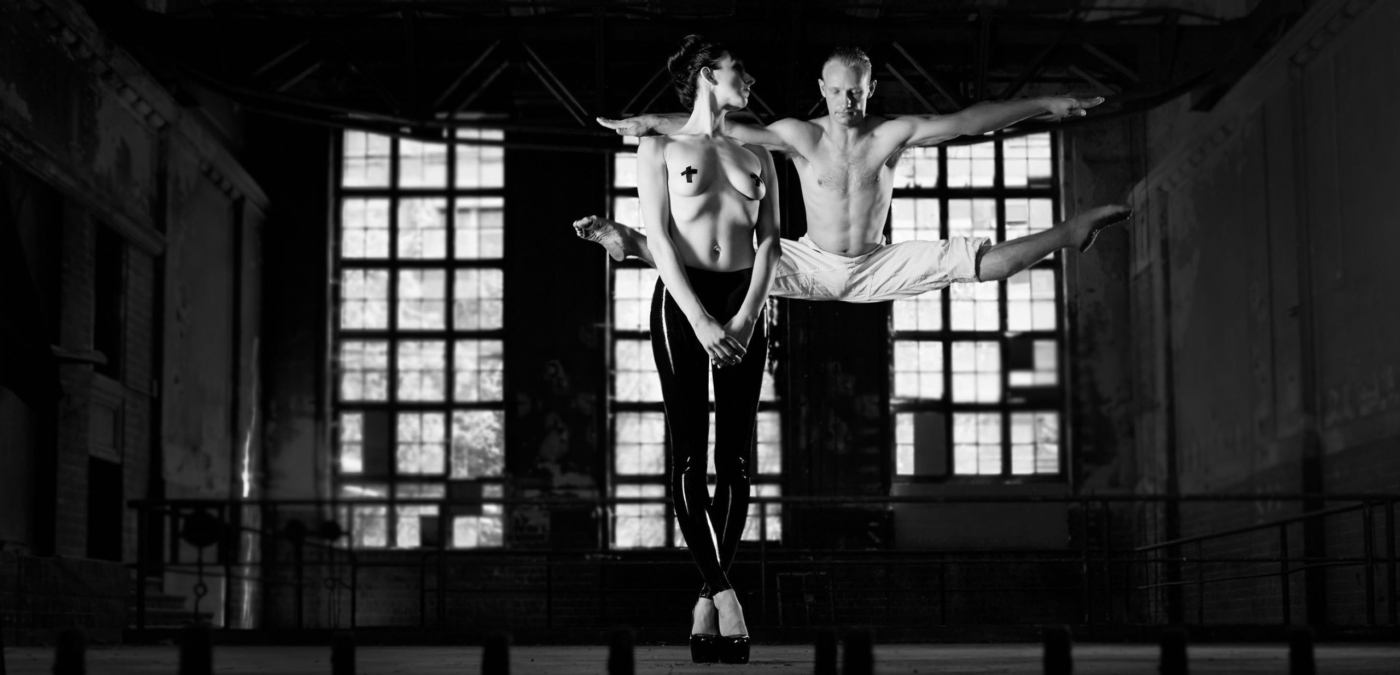 Frau stehend Halbakt mit verdeckten Nippel dahinter ein Tänzer in der Luft im Spagat schwarz weiss in einem Lostplace